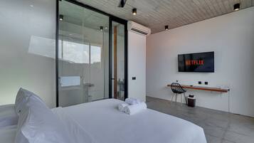 A modern hotel room with a bed, a desk, a chair, a TV, and an air conditioning unit.