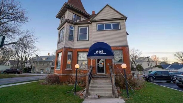 A two-story building with a prominent entrance, a sign reading '802 East Grove,' and a staircase leading to the door.