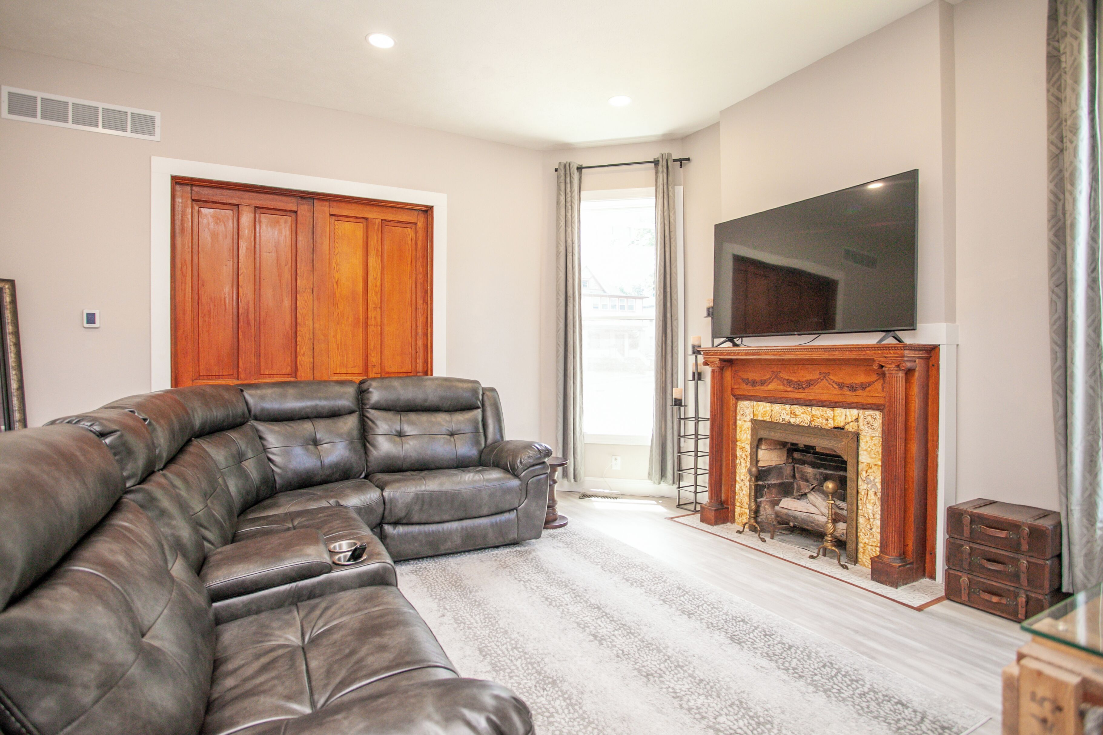 A living room with a leather sofa, a flat-screen TV, a fireplace, and a wooden door.