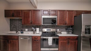 A modern kitchen with stainless steel appliances, wooden cabinets, and a tiled backsplash.