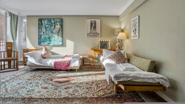 Een kamer met twee bedden, een groot schilderij, een spiegel en een kamerbreed tapijt.