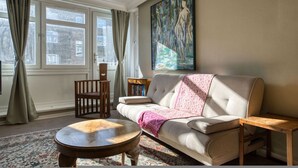 Een woonkamer met een bank, een houten tafel, een stoel, een boekenkast en een groot schilderij aan de muur.