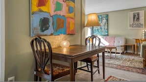 Een eetruimte met een houten tafel, stoelen en een kleurrijk abstract schilderij aan de muur.