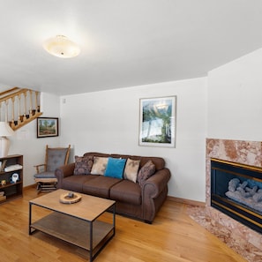 A living room with a brown sofa, a wooden coffee table, a bookshelf, a framed picture, and a fireplace. - Alpine Escape (South Lake Tahoe)