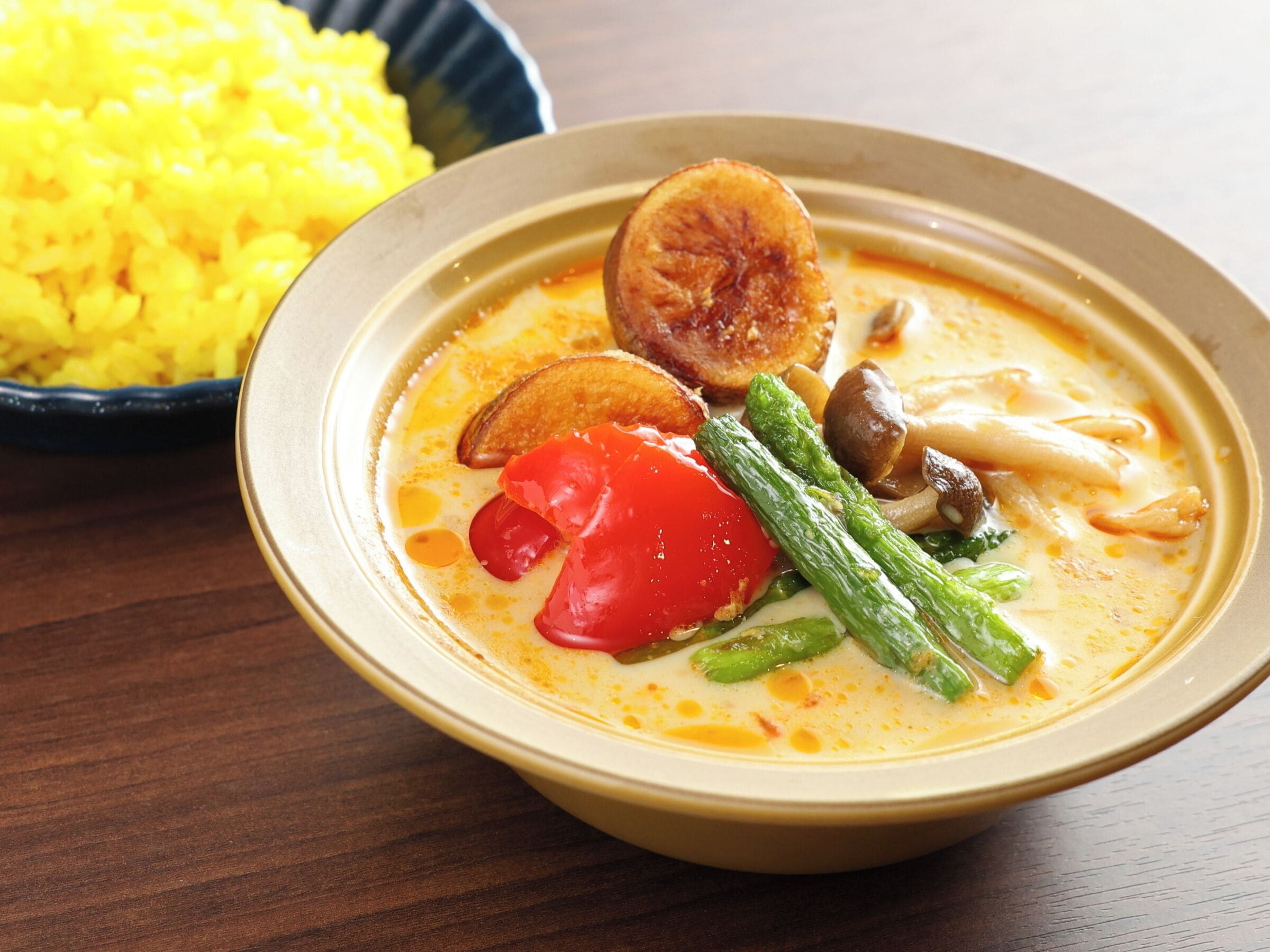 A bowl of soup with vegetables and a side of yellow rice.