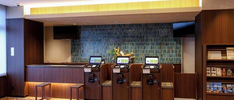 A reception area with a wooden floor, a reception desk, two computer kiosks, a wall with a blue mosaic pattern, and a bookshelf with magazines.