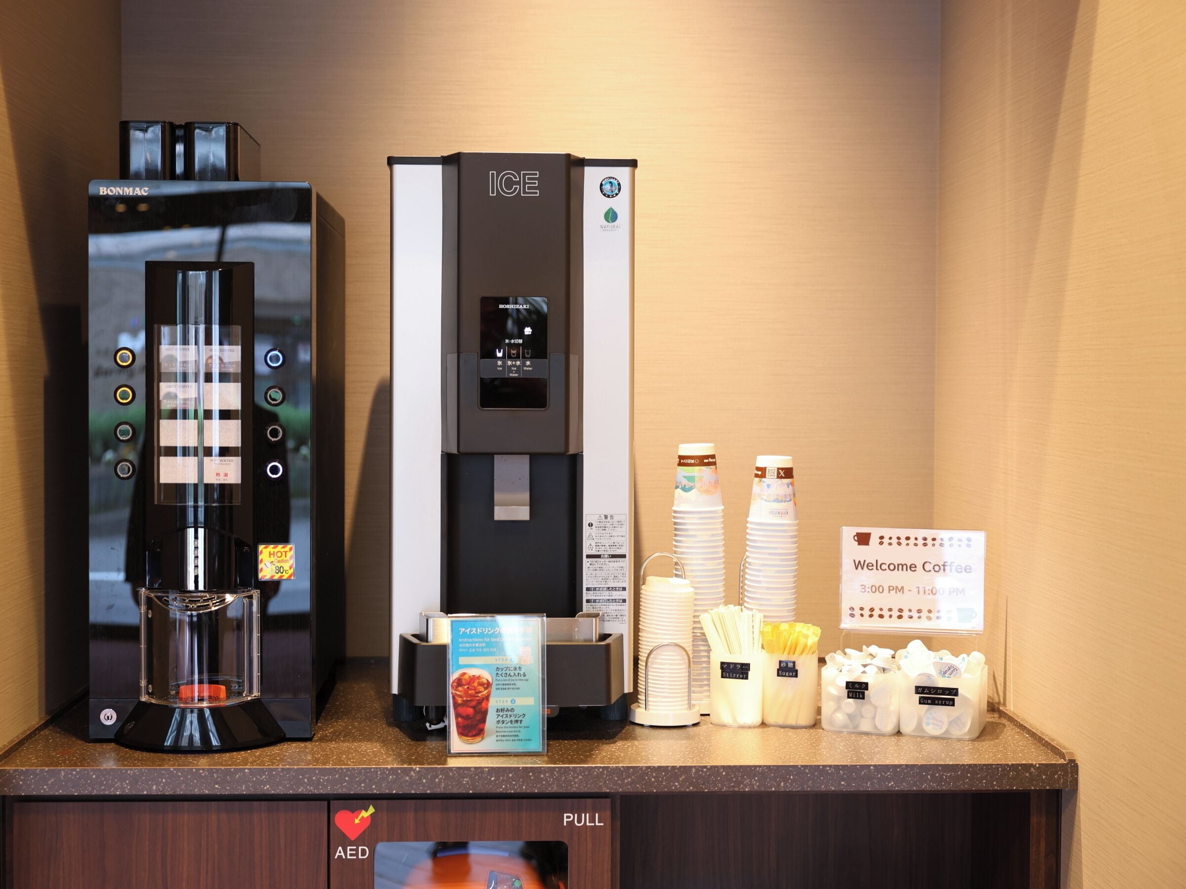 Una estación de café con una máquina de café Bonmac, un dispensador de agua helada y un letrero que da la bienvenida a los visitantes al área de café.