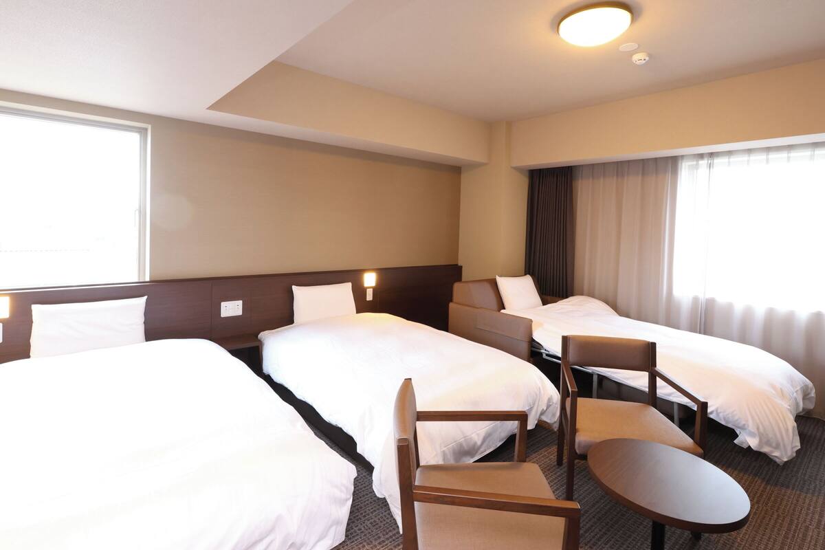 Habitación de hotel con tres camas, un escritorio y una silla.