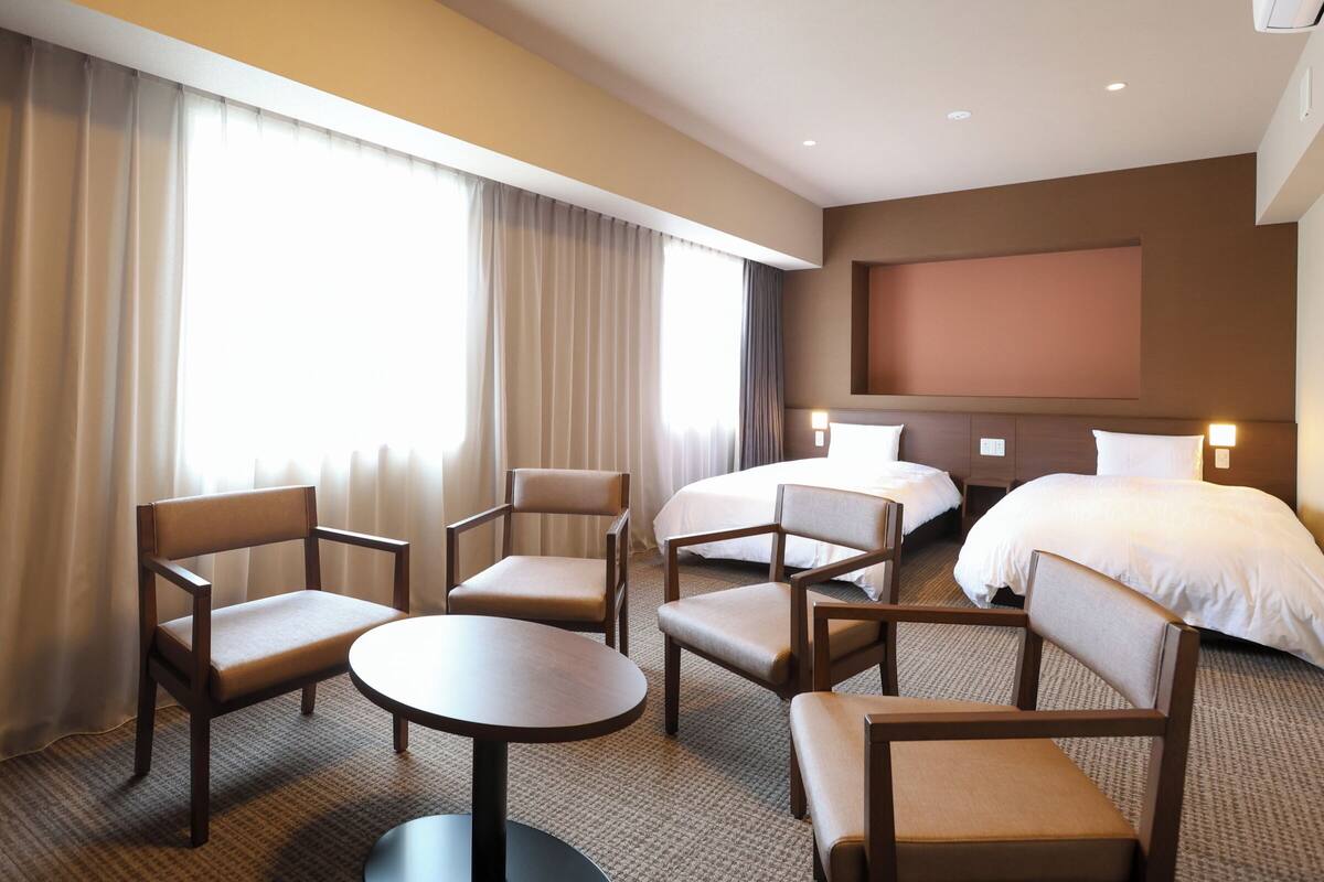 Habitación de hotel con dos camas, televisor y zona de estar con una mesa.