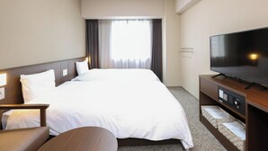 Ein Hotelzimmer mit einem großen Bett, einem Flachbildfernseher, einem Schreibtisch mit Stuhl und einem Fenster mit Vorhängen.