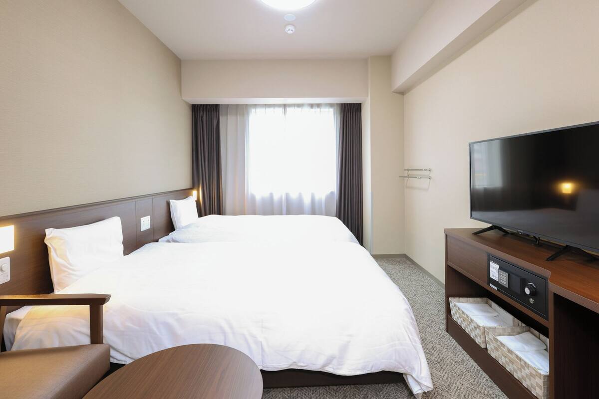 Habitación de hotel con una cama grande, un televisor de pantalla plana, un escritorio con silla y una ventana con cortinas.