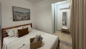 A bedroom with a bed, a bedside table, a lamp, a painting, and a bathroom visible through an open door. - Modern 4BR Apartment Near SJU Airport | Fast WiFi • Parking - AC (San Juan)