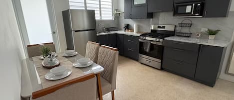 A modern kitchen with dark cabinets, a stainless steel refrigerator, a microwave, a stove, and a dining area with a table set for two.