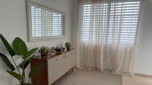 A room with a large window, a wooden cabinet, and a potted plant. - Modern 4BR Apartment Near SJU Airport | Fast WiFi • Parking - AC (San Juan)