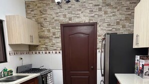 Cuina amb respatller de pedra, porta marró fosc, nevera i armaris de fusta.