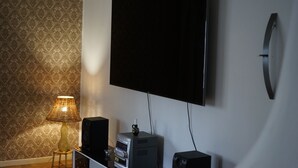 Ein Zimmer mit Flachbildfernseher an der Wand, einem kleinen Tisch mit Lampe und einem Lautsprecher.