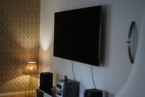 Ein Zimmer mit Flachbildfernseher an der Wand, einem kleinen Tisch mit Lampe und einem Lautsprecher.