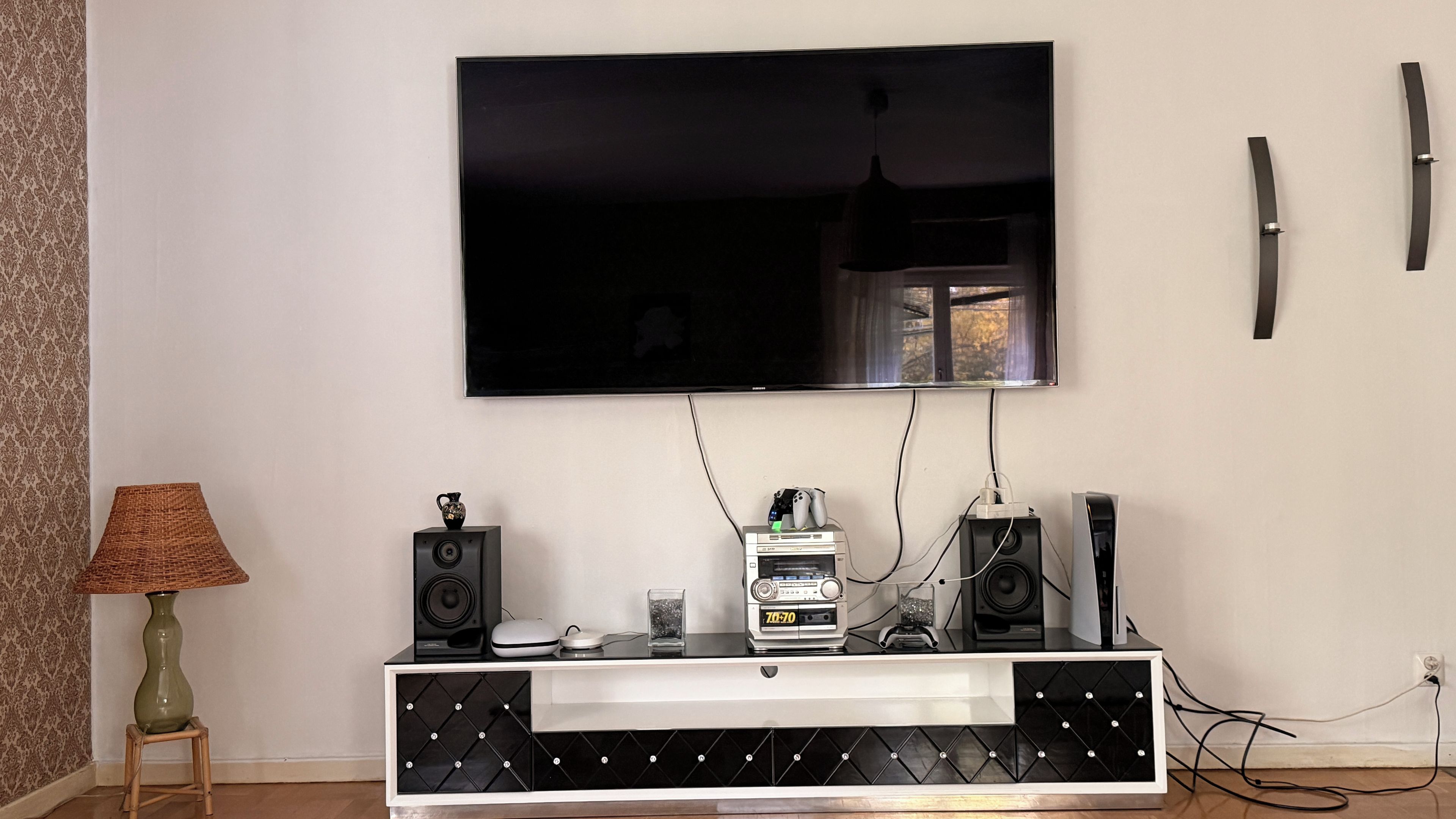 A modern living room with a flat-screen TV mounted on the wall, a black and white entertainment unit below, and a lamp on a side table.