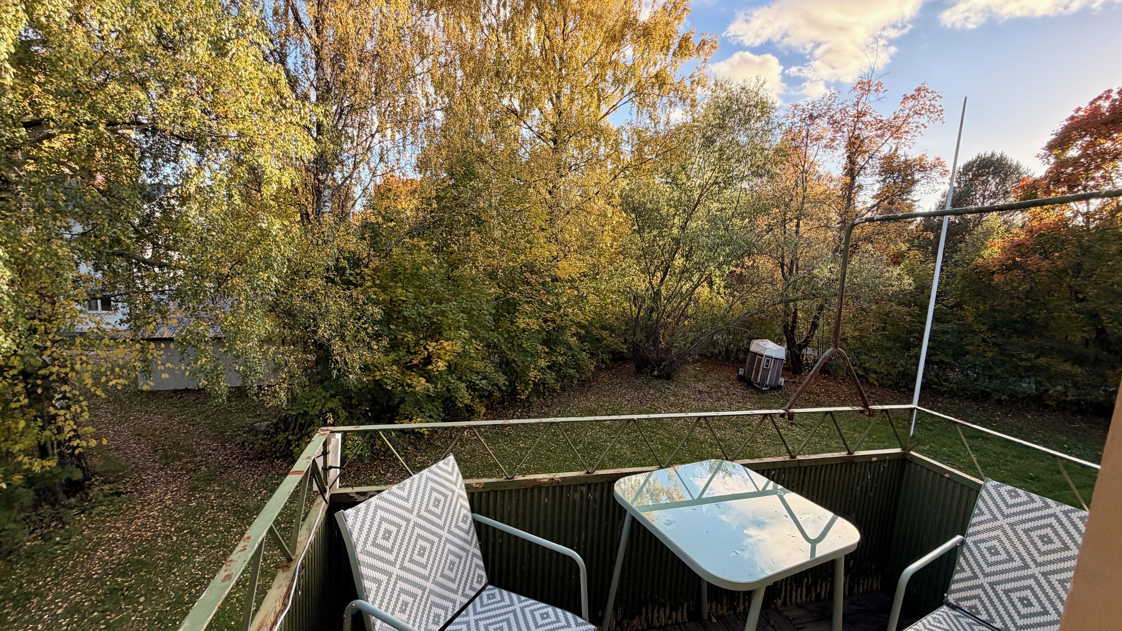 Un espace extérieur aménagé en terrasse, avec une table et des chaises, entouré d’arbres et d’un petit abri de jardin.