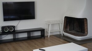 Ein Wohnzimmer mit Flachbildfernseher, weißem Tisch, weißem Sessel, schwarzem Unterhaltungsschrank und Kamin aus Ziegelsteinen.