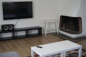 Ein Wohnzimmer mit Flachbildfernseher, weißem Tisch, weißem Sessel, schwarzem Unterhaltungsschrank und Kamin aus Ziegelsteinen.