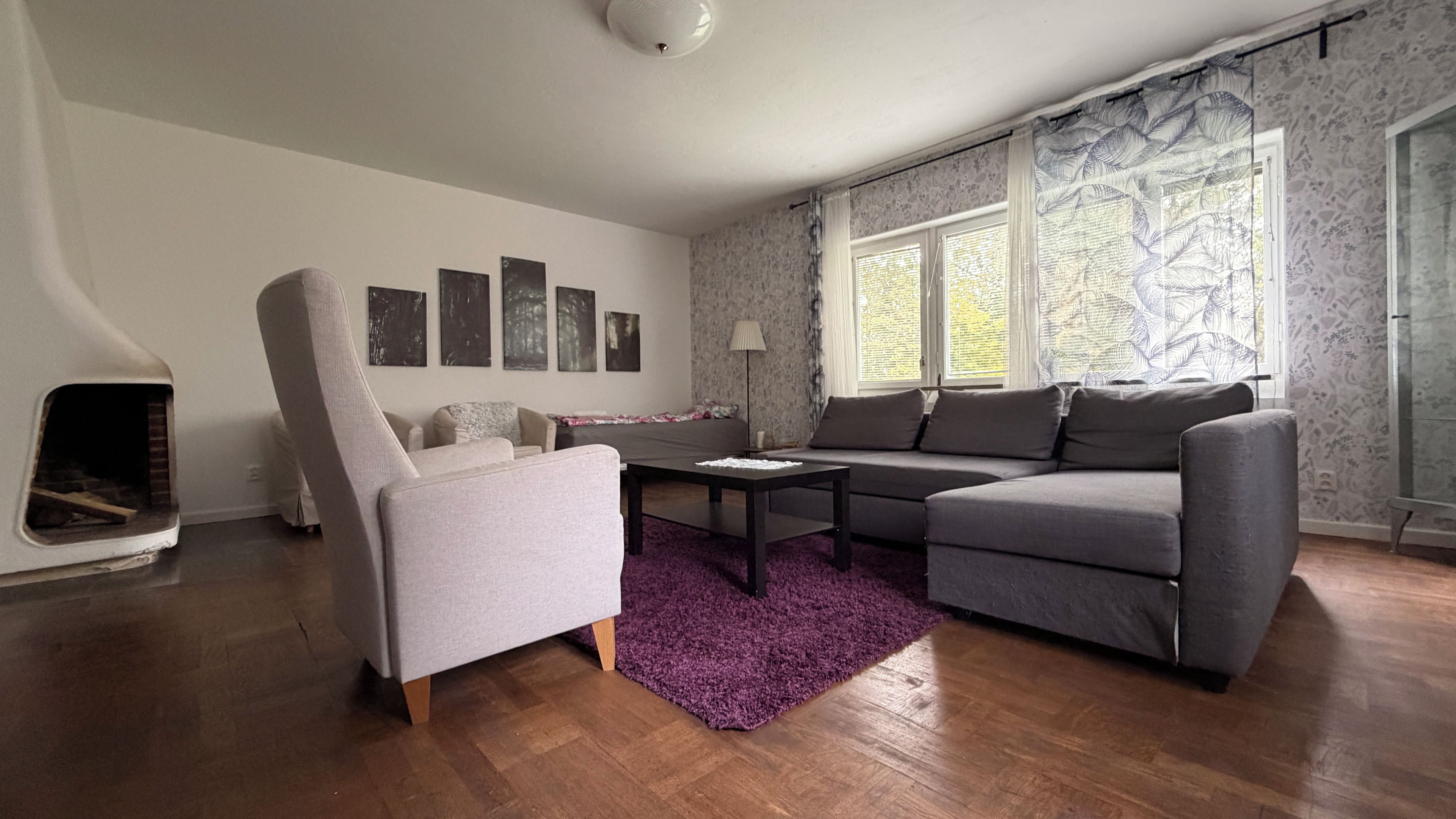 A living room with a sofa, armchair, coffee table, fireplace, and artwork on the wall.