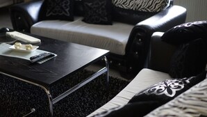 Ein Wohnzimmer mit einem schwarzen Couchtisch, einem weißen Sofa mit gemusterten Kissen und einer Fernbedienung auf dem Tisch.