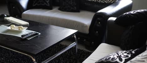 A living room with a black coffee table, a white sofa with patterned cushions, and a remote control on the table.