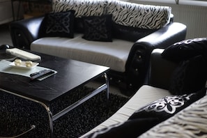 A living room with a black coffee table, a white sofa with patterned cushions, and a remote control on the table.