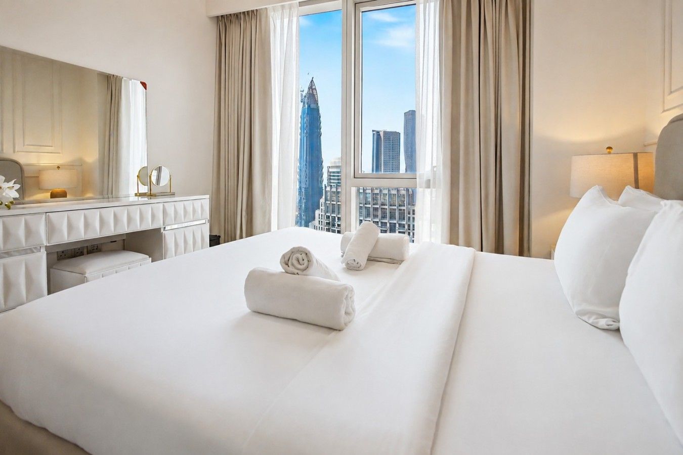 Une chambre d’hôtel avec un grand lit, une coiffeuse avec un miroir et une vue sur les bâtiments de la ville par la fenêtre.