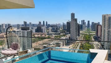 Piscina infinita en la azotea con vista a la ciudad, un sillón colgante y un cielo despejado.