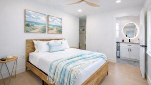 Un dormitorio con cama, mesita de noche, ventilador de techo y una obra de arte en la pared.