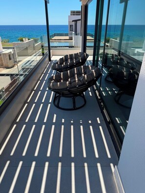 Ein Balkon mit zwei schwarzen Sitzgelegenheiten, einer Glastrennwand und Blick aufs Meer.