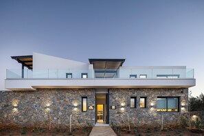 Ein modernes, zweistöckiges Haus mit Natursteinfassade, einem Glasbalkon und einem Weg zum Eingang.