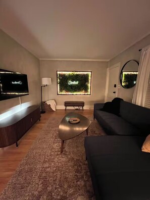 A modern living room with a flat-screen TV, a sofa, a coffee table, and a wall-mounted TV. - Boutique Cleveland Vibe - Neon Moss Wall - King Bed - Queen Bed (Lakewood)