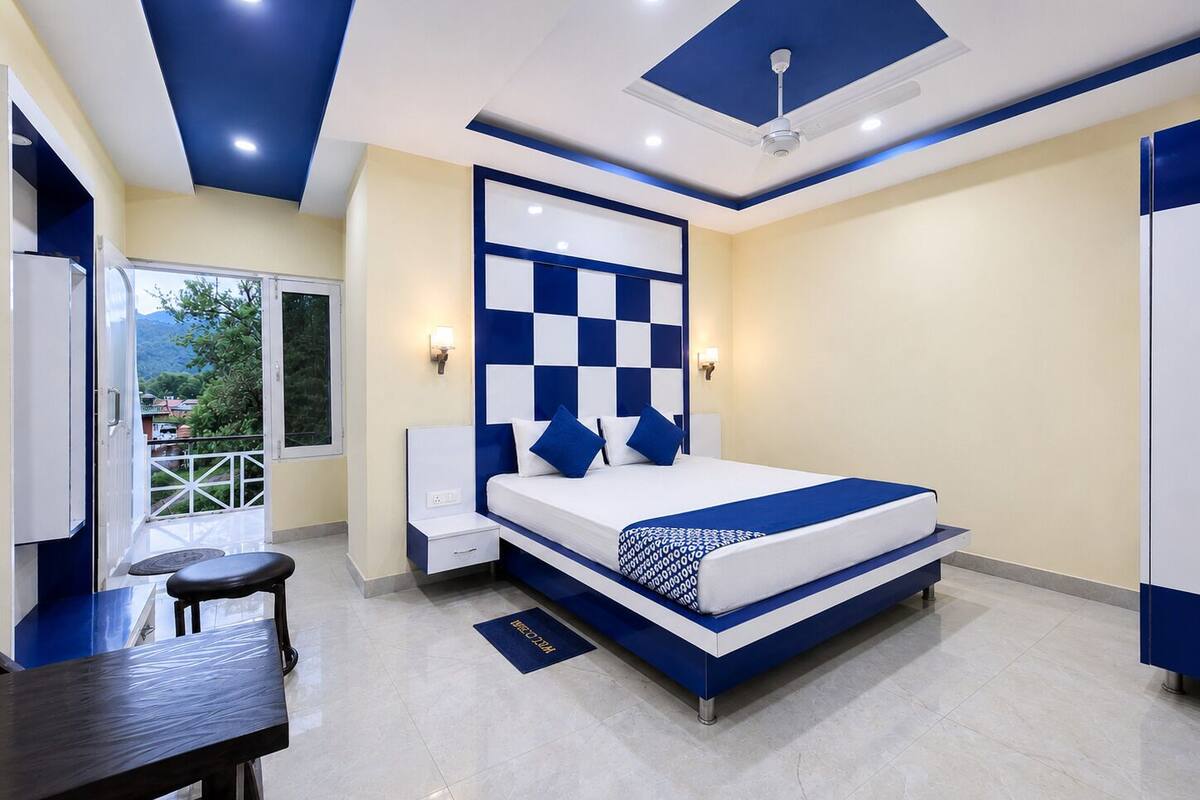 A modern bedroom with a checkered headboard, a bed with blue and white bedding, a desk with a chair, and a balcony with a view.