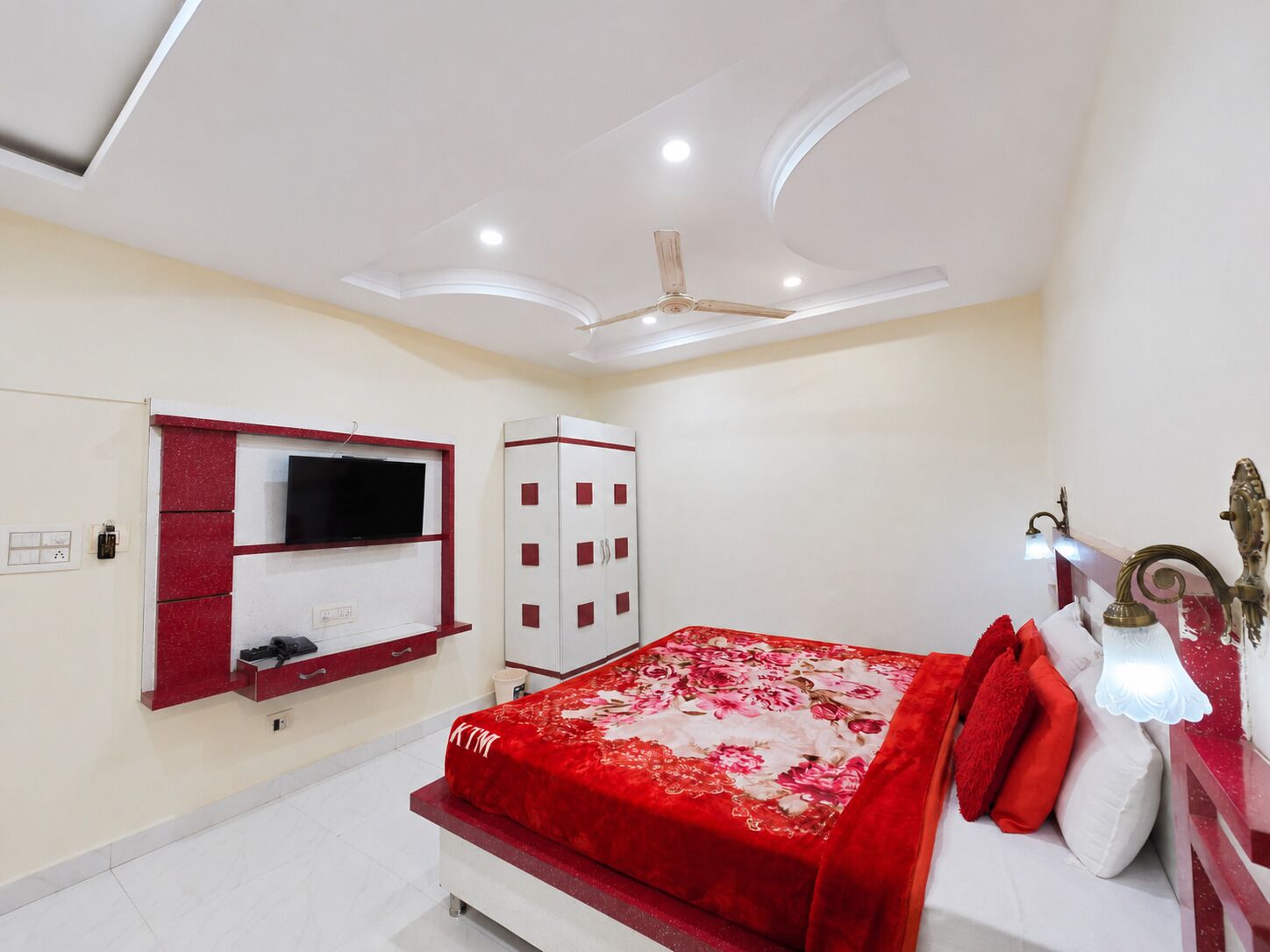 A bedroom with a bed, a TV mounted on the wall, a wardrobe, and a ceiling fan.