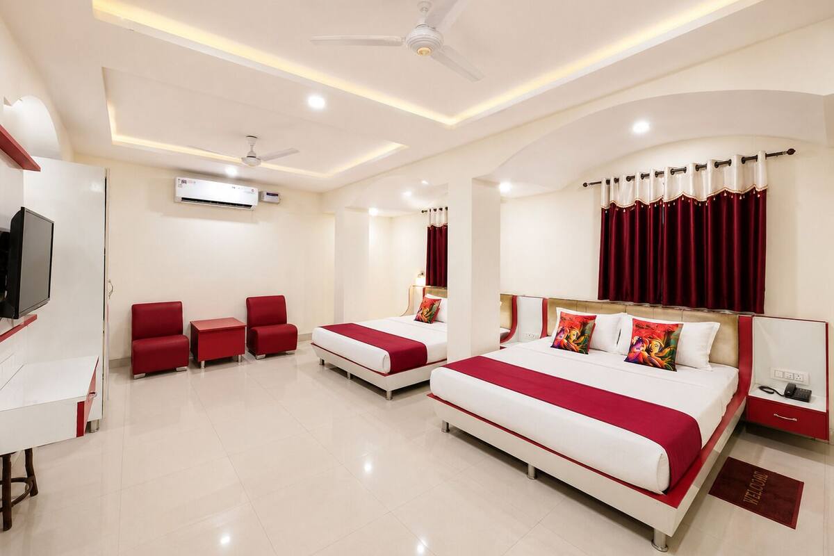 A hotel room with a large bed, two smaller beds, a desk, a TV, and a ceiling fan.