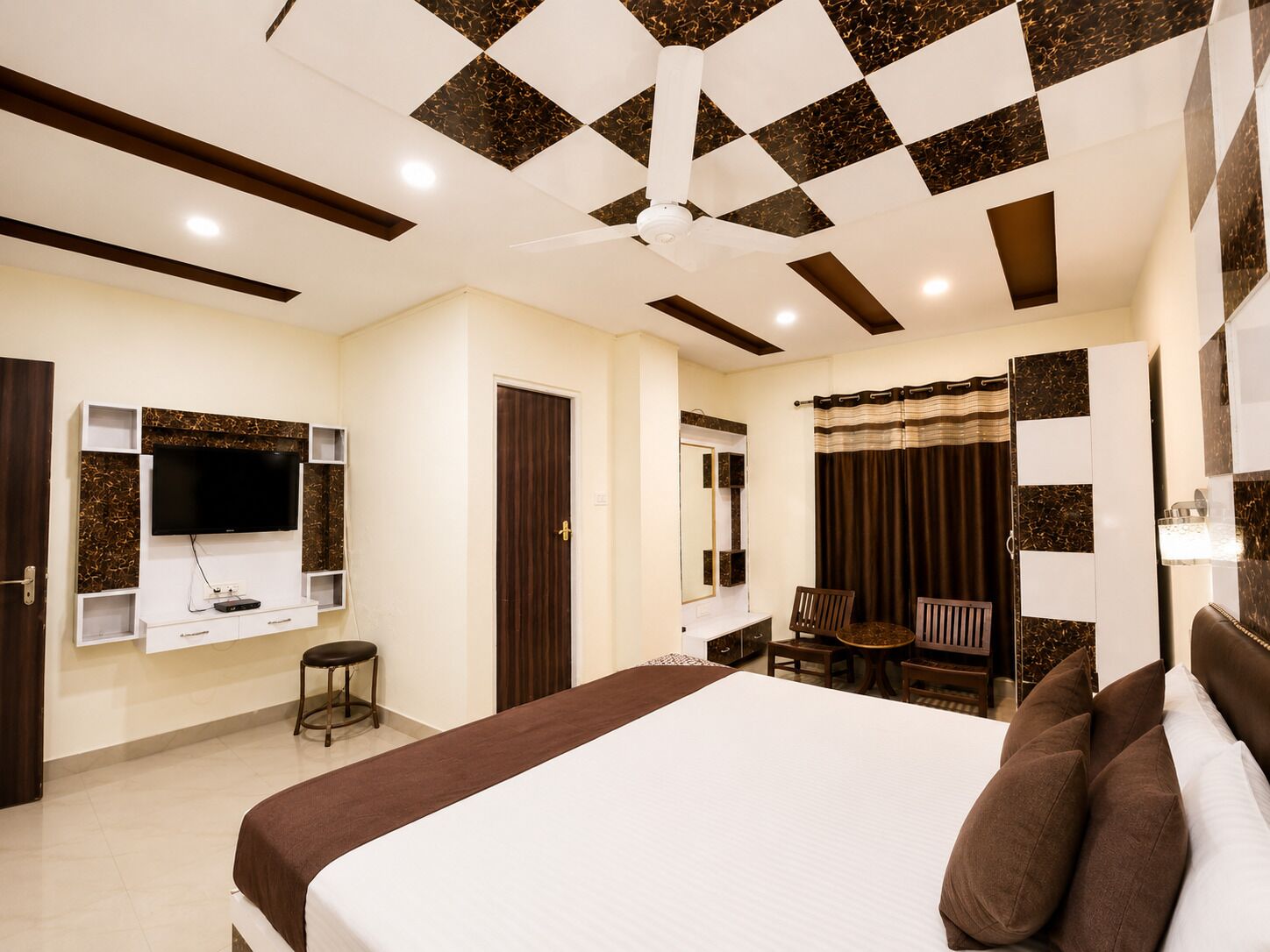 Quarto de hotel com uma cama grande, televisão na parede, mesa com cadeira e banheiro com espelho e cortinas.