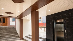 A modern building interior with a staircase, elevator, and a hallway leading to a door. - Osho Hotel, Restaurant & Banquet (Palampur)