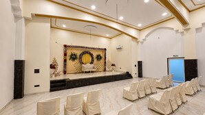 A conference room with a stage, rows of chairs, and a blue door. - Osho Hotel, Restaurant & Banquet (Palampur)