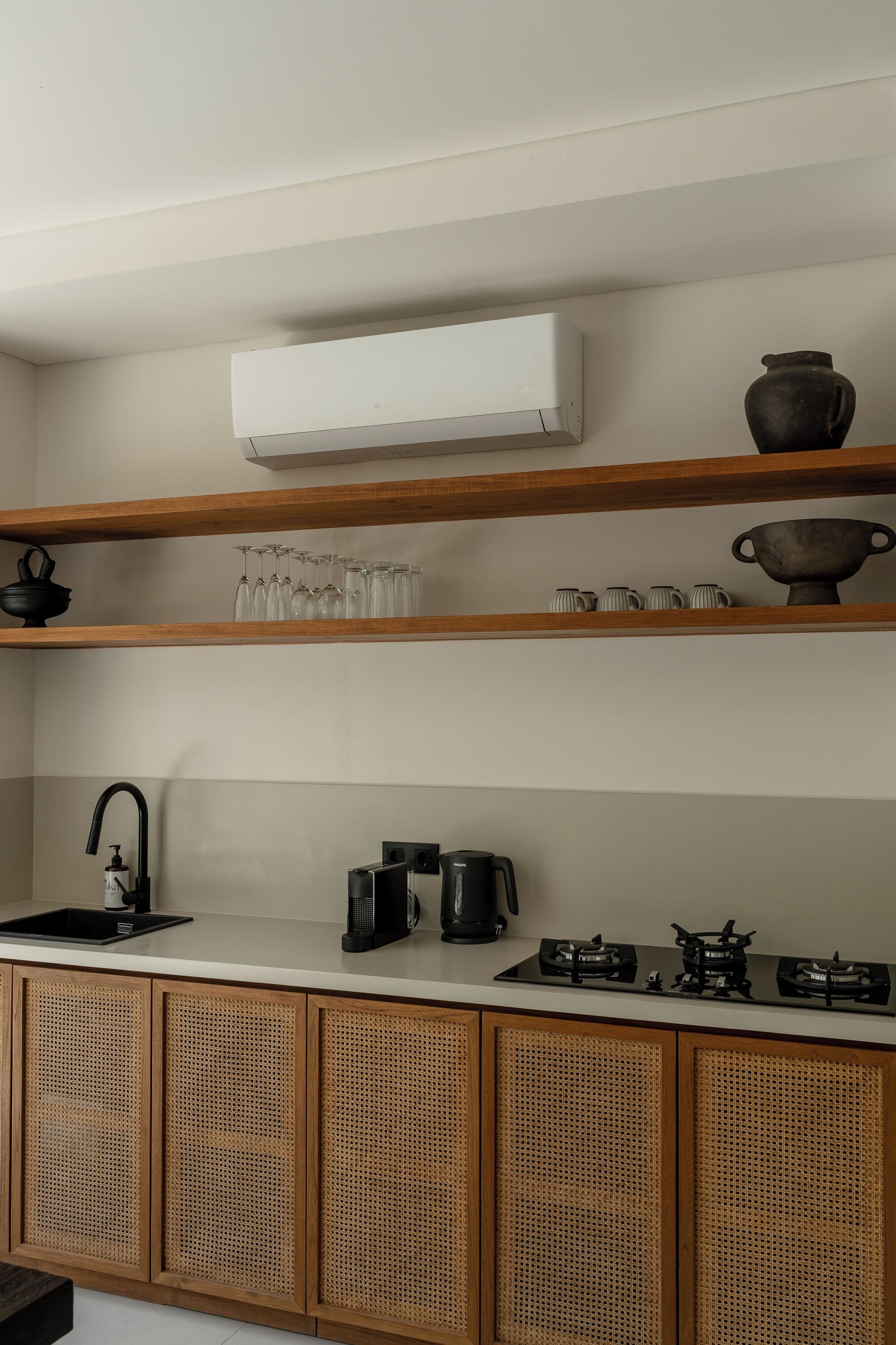 A kitchen with a white countertop, wooden cabinets, a black faucet, a coffee maker, a kettle, and a stove.