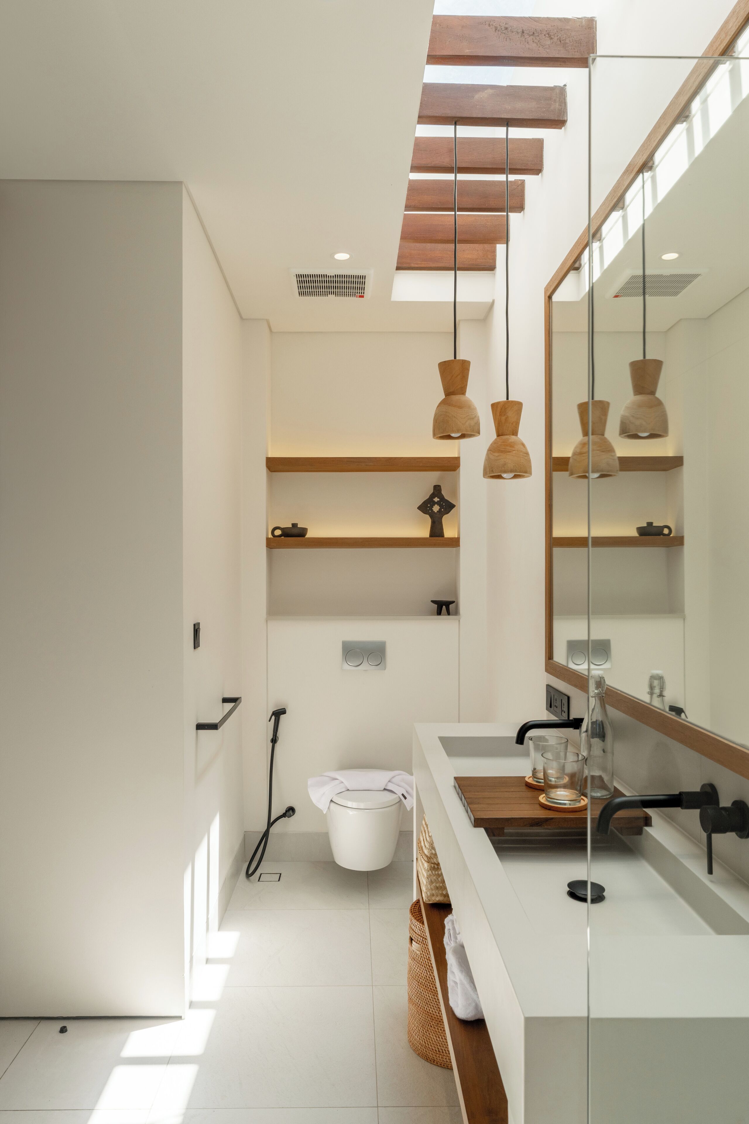 Un baño moderno con un lavamanos blanco, estantes de madera, un espejo grande y luces colgantes.