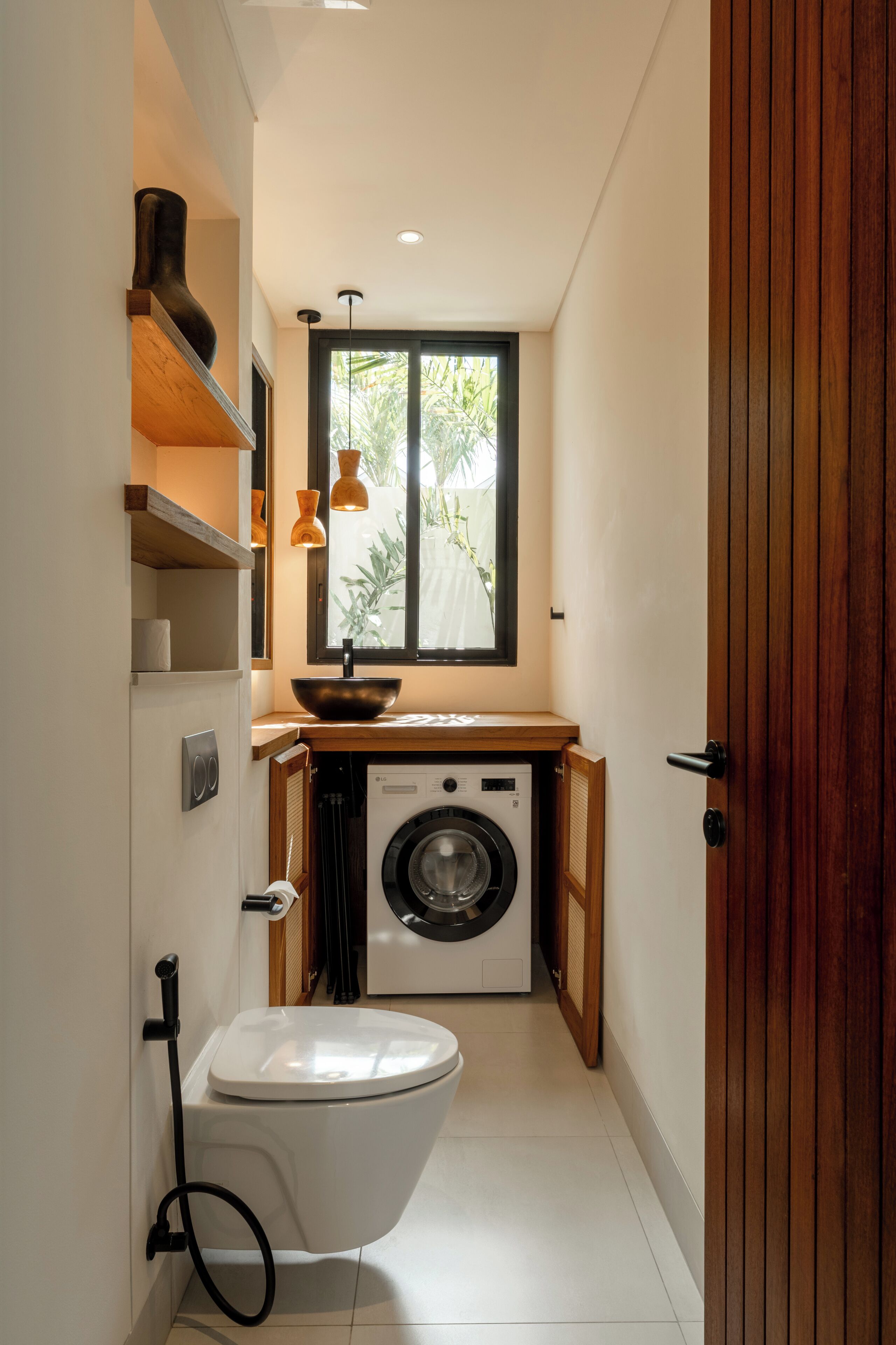 A compact bathroom with a toilet, washing machine, and a window providing natural light.
