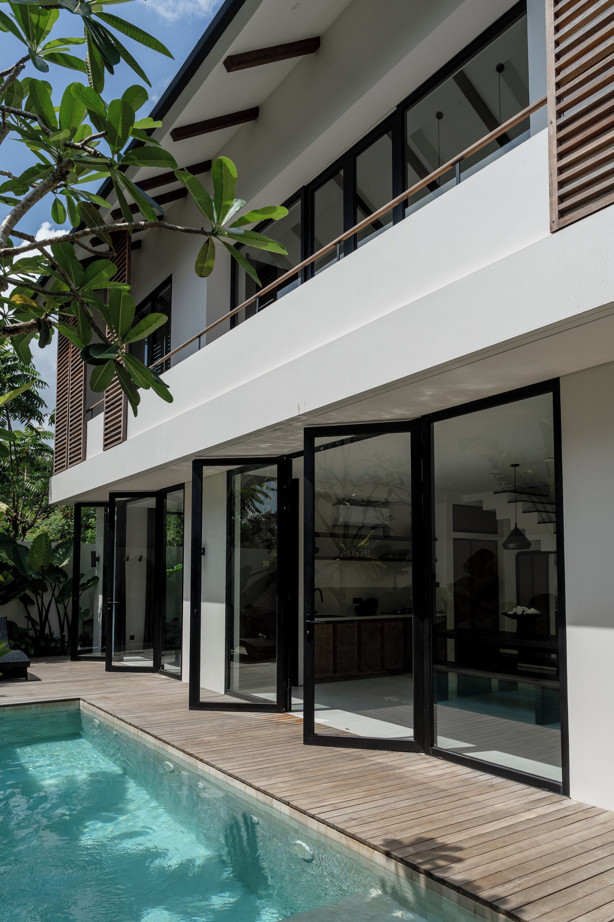 A modern two-story house with a swimming pool, large glass doors, and a wooden deck.