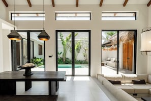 Un intérieur moderne avec une table à manger, un canapé et de grandes fenêtres donnant sur un espace piscine.