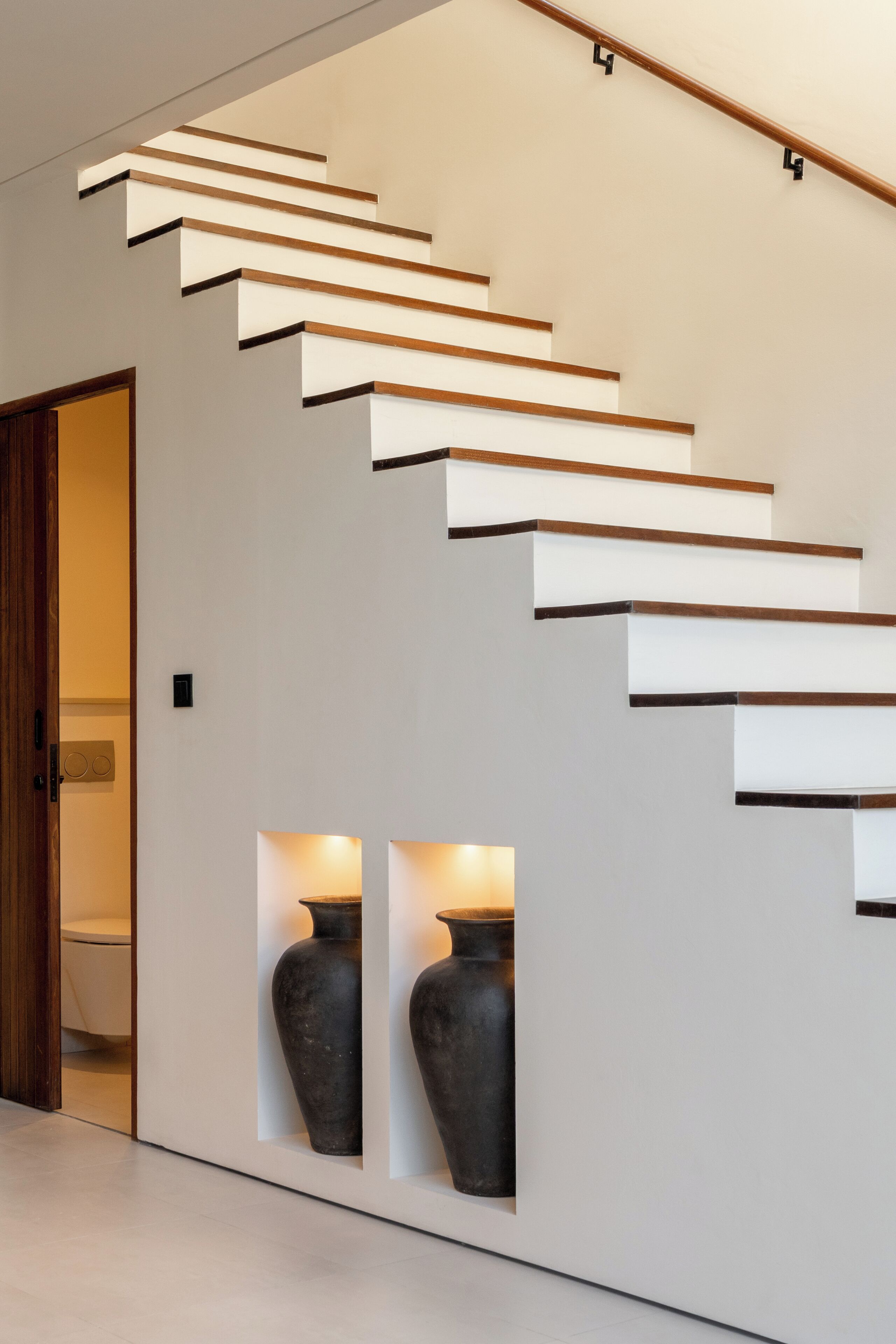 Una escalera moderna con barandilla de madera y peldaños blancos.