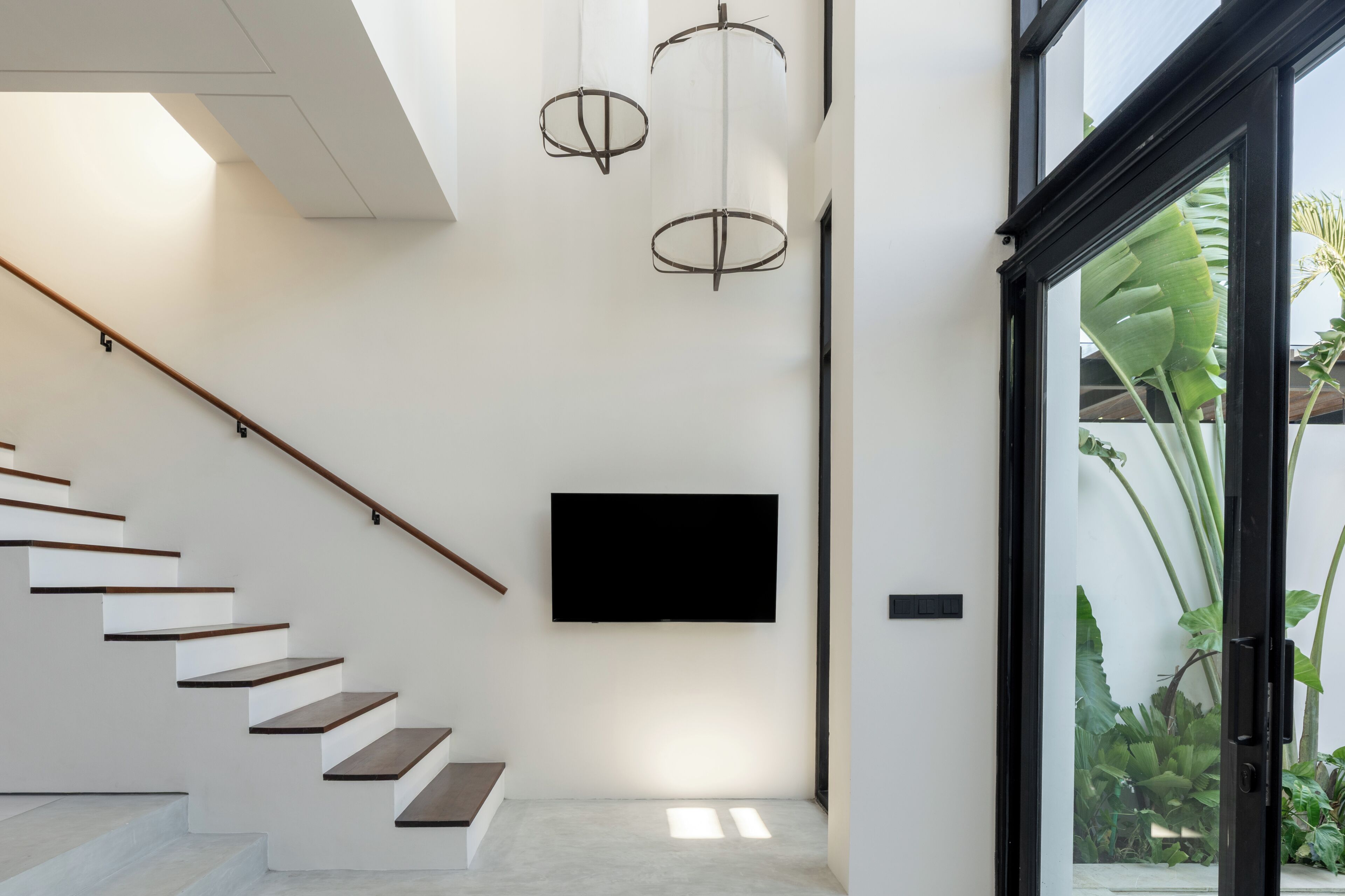 Una escalera moderna de diseño minimalista, un televisor de pantalla plana montado en la pared y un ventanal con vistas a zonas verdes.