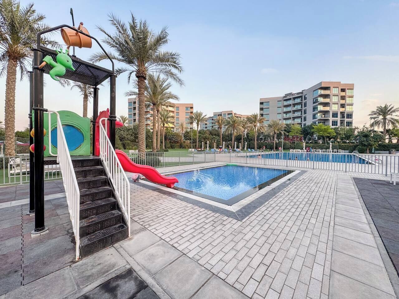 A swimming pool area with a red slide, a children's play structure, and a staircase leading to a deck.