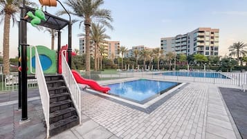 A swimming pool area with a red slide, a children's play structure, and a staircase leading to a deck.